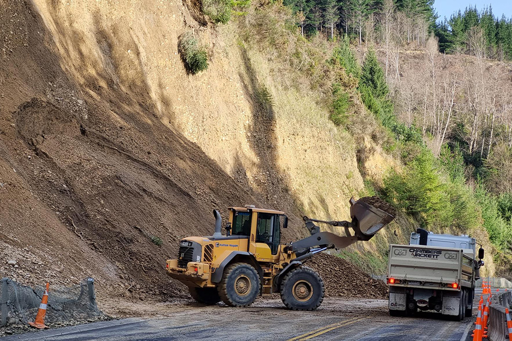 Digger and trucks working on a road that suffered a landslide