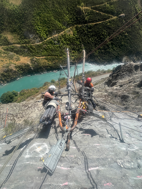 Two workers abseiling high up on a cliff face with the river far below them