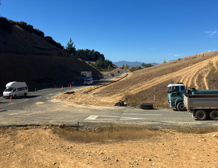 Image of truck on road with hill in background, close to intersection construction area.
