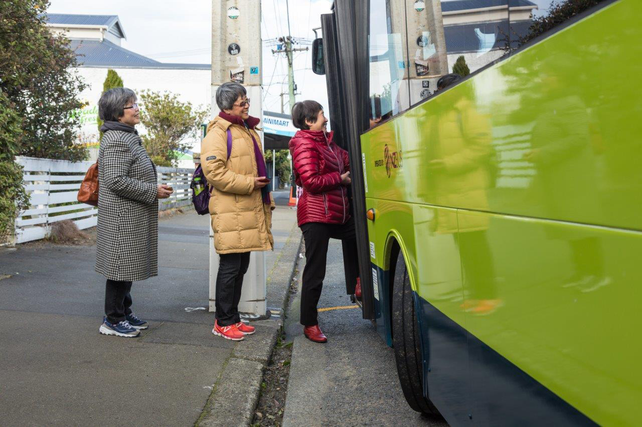 Three women wearing winter jackets boarding a bus at bus stop