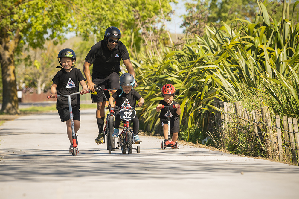 Man and children riding bikes and scooters along path