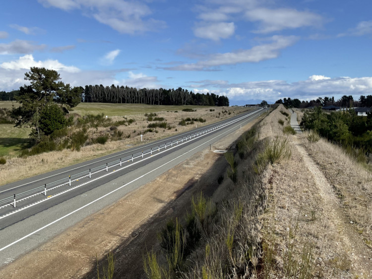 A motorway bordered by a grassy field on one side and a road on the other, featuring a safety barrier for protection.