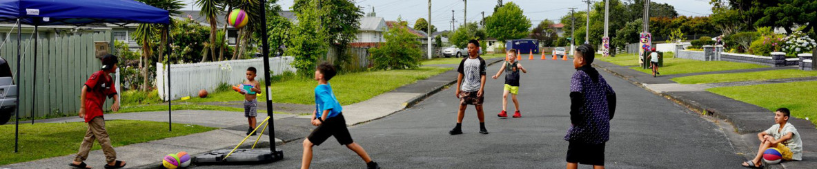 children playing neighbourhood basketball in the middle of street which is cordoned off by orange cones